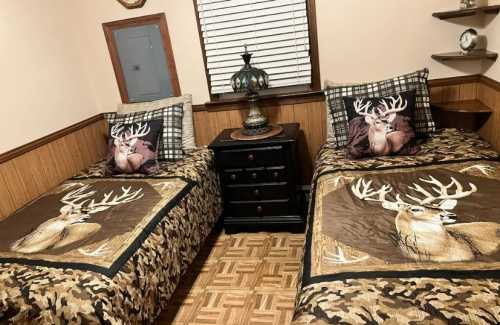 A cozy bedroom with two twin beds, each featuring deer-themed bedding and decorative pillows, and a nightstand in between.