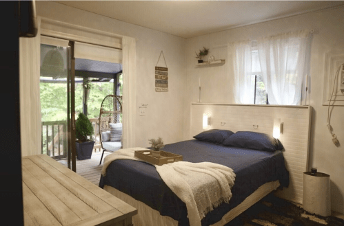 Cozy bedroom with a blue bedspread, wooden furniture, and a sliding door leading to a balcony with greenery outside.