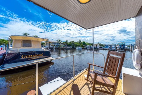 A wooden rocking chair on a deck overlooking a calm waterway with boats and blue skies in the background.