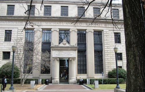 Exterior view of a grand library building with large columns and a central entrance, surrounded by trees.