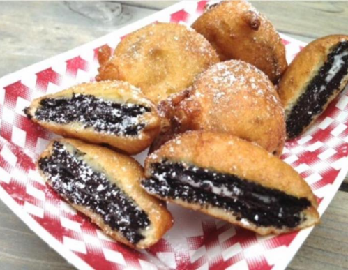 Fried Oreos dusted with powdered sugar, cut in half to reveal the creamy filling inside.
