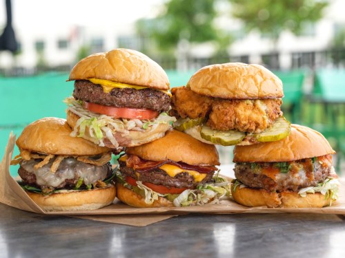 A stack of delicious burgers with various toppings, including cheese, lettuce, tomato, and pickles, on a wooden surface.