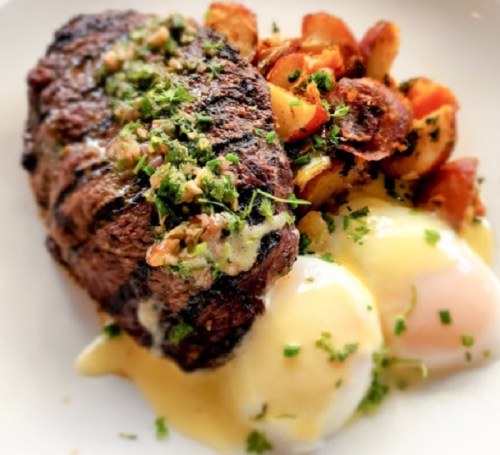 A plate featuring grilled steak topped with herbs, alongside roasted potatoes and two poached eggs with hollandaise sauce.