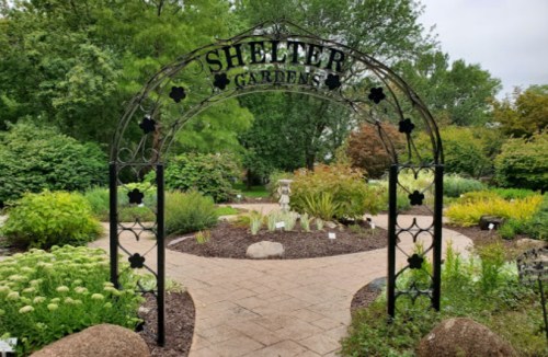 A decorative archway labeled "Shelter Garden" leads into a lush, green garden filled with various plants and pathways.