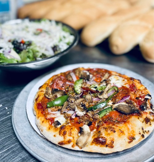 A freshly baked pizza topped with mushrooms, green peppers, and onions, served with a side salad and breadsticks.