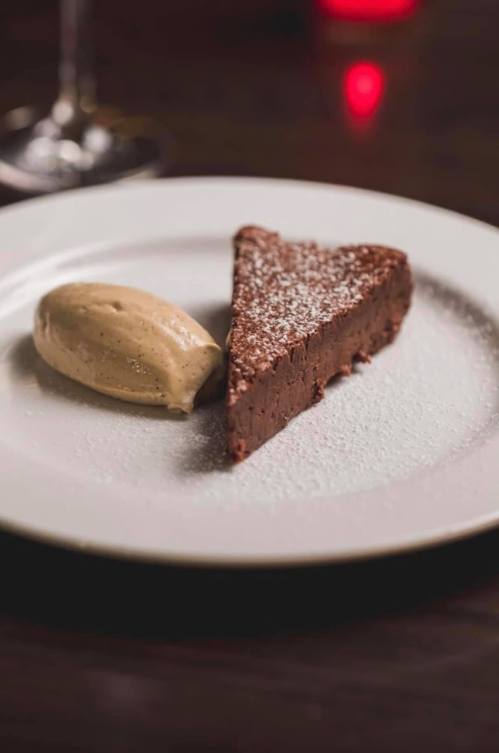 A slice of rich chocolate cake dusted with powdered sugar, served with a scoop of creamy caramel ice cream.