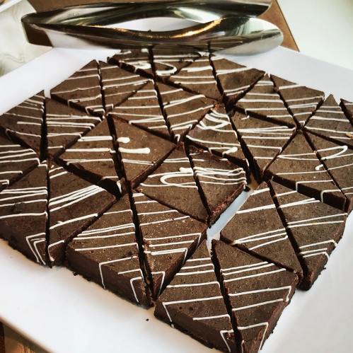 A plate of triangular chocolate brownies drizzled with white icing, arranged neatly in a grid pattern.