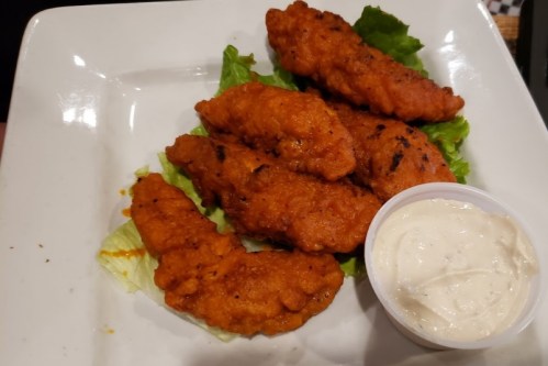 A plate of crispy fried chicken tenders on lettuce, served with a small cup of dipping sauce.