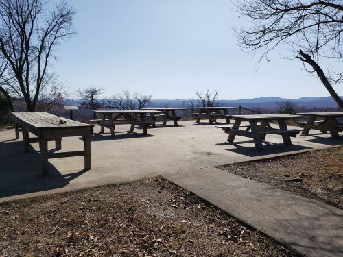 A spacious outdoor area with wooden picnic tables and a scenic view of distant mountains under a clear blue sky.