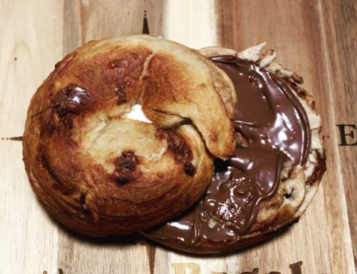 A toasted bagel half spread with chocolate hazelnut spread on a wooden surface.