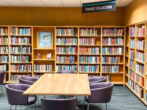 A library interior featuring bookshelves filled with books, a table, and a sign reading "Chavez Collection."