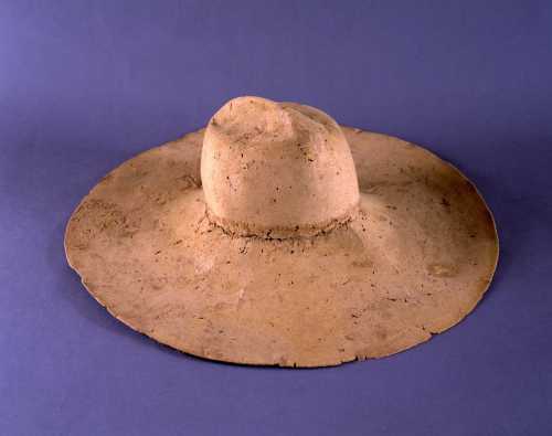 A wide-brimmed, light-colored hat made of a textured material, displayed against a purple background.