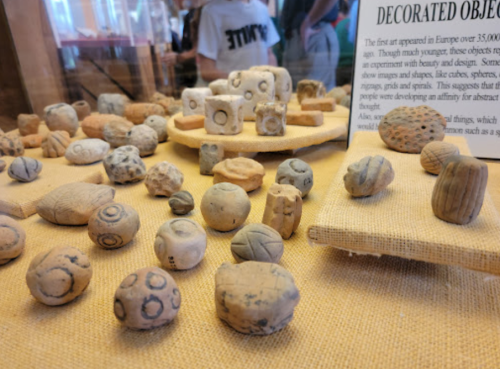 A display of ancient decorated objects, including various shaped stones and clay artifacts, on a textured surface.