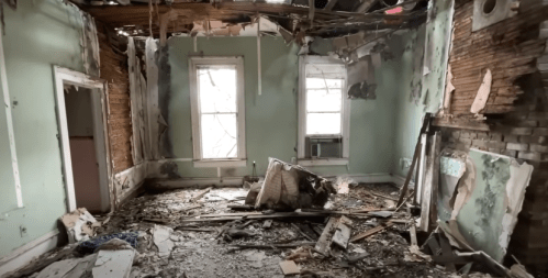 A dilapidated room with peeling walls, debris on the floor, and broken windows, showcasing signs of neglect and decay.
