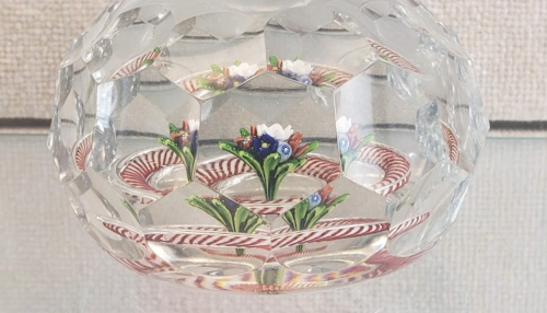 A decorative glass paperweight featuring intricate floral designs and a striped base.