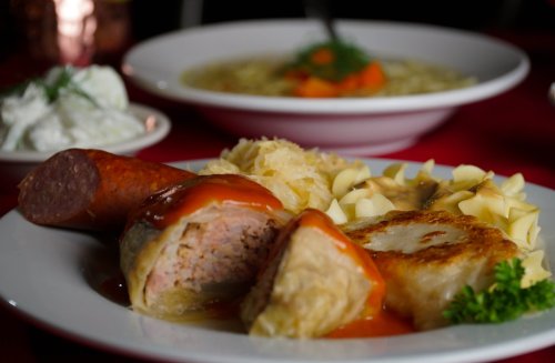 A plate of hearty food featuring sausage, stuffed cabbage, noodles, sauerkraut, and a side of creamy dip.