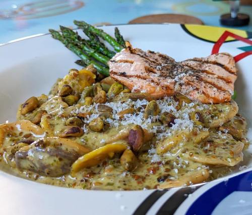 A plate of creamy pasta with mushrooms and pistachios, topped with grilled salmon and asparagus.