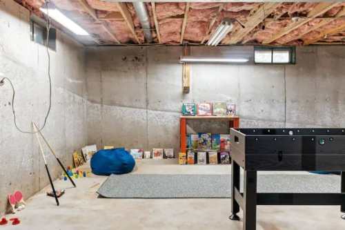 A spacious basement with exposed beams, a foosball table, a blue bean bag, and shelves filled with books.