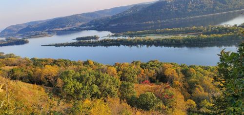 A scenic view of a river winding through lush, colorful autumn foliage and rolling hills under a clear sky.