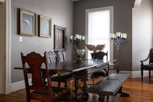 A vintage dining room with a large wooden table, ornate chairs, and decorative wall art, featuring a candelabra and an eagle statue.