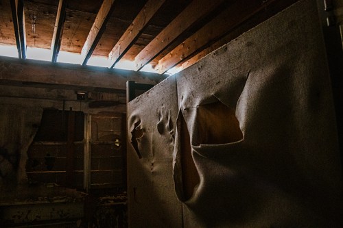 Dimly lit room with peeling walls and sunlight streaming through a gap in the ceiling.