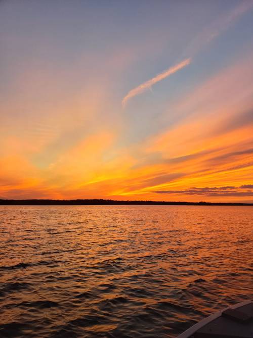 A vibrant sunset over a calm lake, with orange and pink hues reflecting on the water's surface.