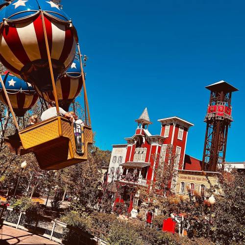 A colorful hot air balloon ride against a clear blue sky, with a whimsical building in the background.