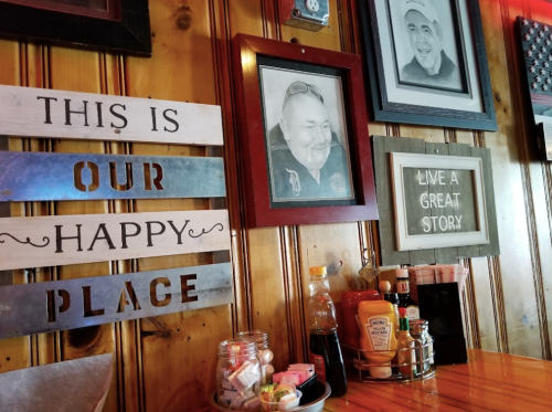 A cozy restaurant wall featuring framed portraits, signs, and condiments on a wooden table.