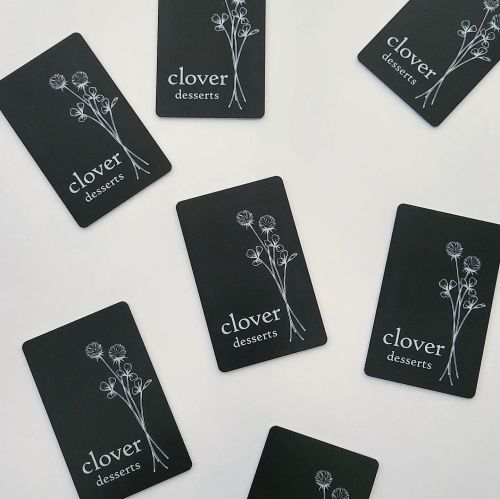 A flat lay of black business cards for "clover desserts" featuring floral illustrations.