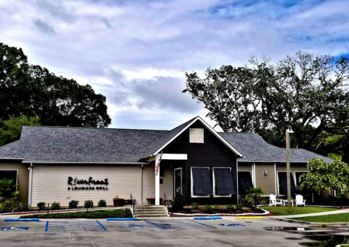 A restaurant building with a dark exterior and light accents, surrounded by trees and a cloudy sky.