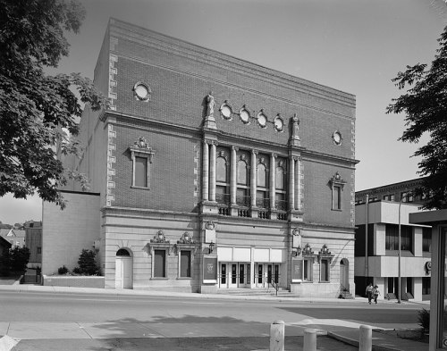 Historic theater building with ornate architecture, large windows, and decorative elements, set in an urban environment.