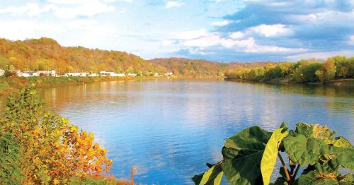 A serene river scene with colorful autumn foliage and a clear blue sky reflecting on the water's surface.