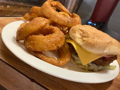 A plate with a cheeseburger topped with lettuce and a side of crispy onion rings.