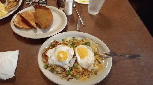 A plate of hash browns topped with two fried eggs, served with toast and a pastry on the side.
