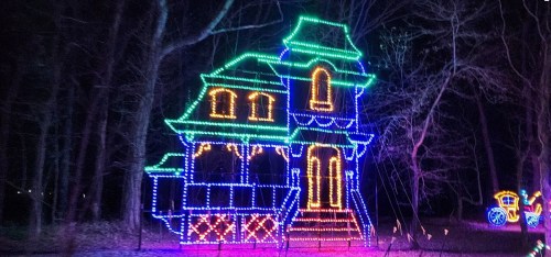 A brightly lit house decorated with colorful lights, surrounded by trees at night.