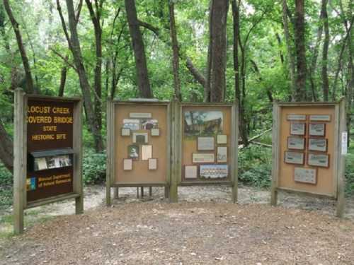 Information display at Locust Creek Covered Bridge historic site, surrounded by trees in a natural setting.