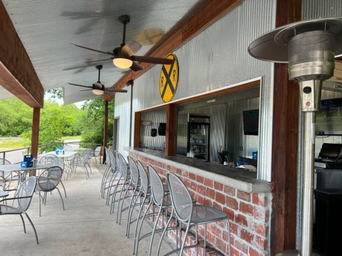 Outdoor bar area with metal roof, brick counter, and seating, featuring a railroad sign and ceiling fans.