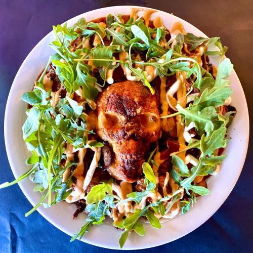 A plate of food shaped like a skull, topped with greens and drizzled with sauce, on a dark background.