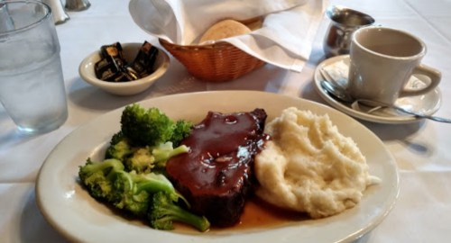 A plate with meatloaf, mashed potatoes, and broccoli, accompanied by a basket of bread and a cup of coffee.