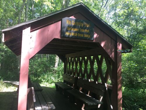 A wooden shelter at the Vin Grimley Trail in Burlington State Park, surrounded by lush greenery.