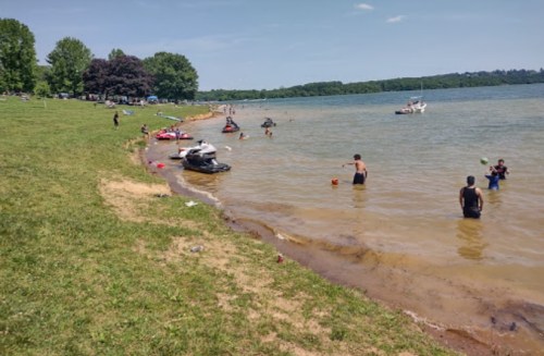 People enjoying a sunny day at the lake, with jet skis, boats, and children playing in the water.