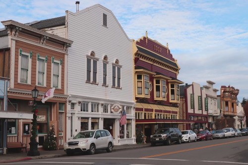 Colorful historic buildings line a street, showcasing unique architectural styles and storefronts in a small town.