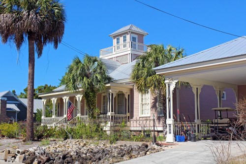 A charming coastal house with a tower, surrounded by palm trees and a clear blue sky.