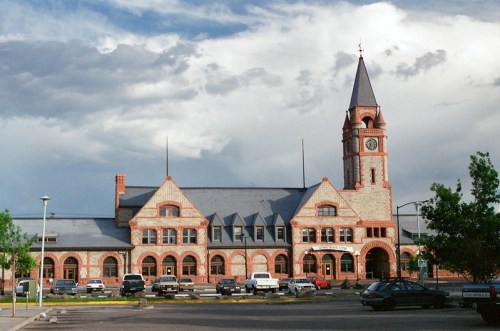 Historic brick building with a clock tower, surrounded by cars and under a cloudy sky.