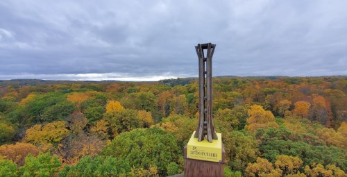 A tall observation tower stands above a vibrant autumn forest under a cloudy sky.