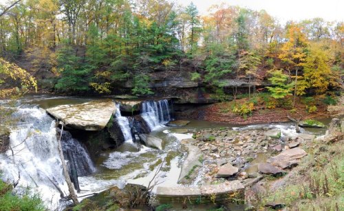 A scenic waterfall surrounded by autumn foliage and rocky terrain, reflecting the beauty of nature in a tranquil setting.