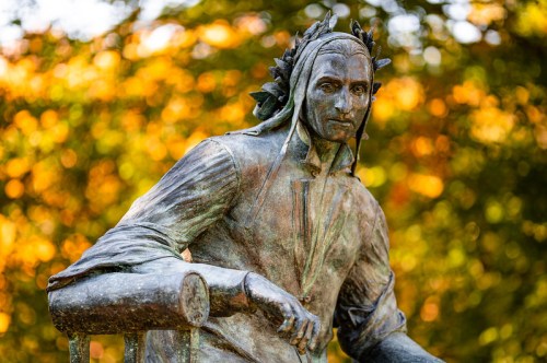 A bronze statue of a man with a laurel wreath, seated against a backdrop of autumn foliage.