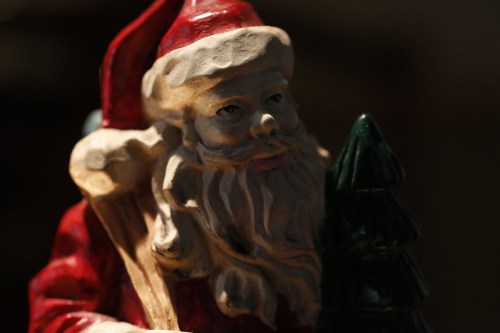 A close-up of a vintage Santa Claus figurine, featuring a detailed face and a small green tree beside him.