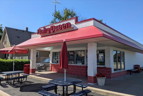 Exterior of a Dairy Queen restaurant with a red awning, picnic tables, and a clear blue sky.