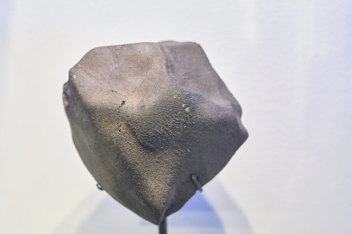 A textured, irregularly shaped rock displayed on a stand against a light background.